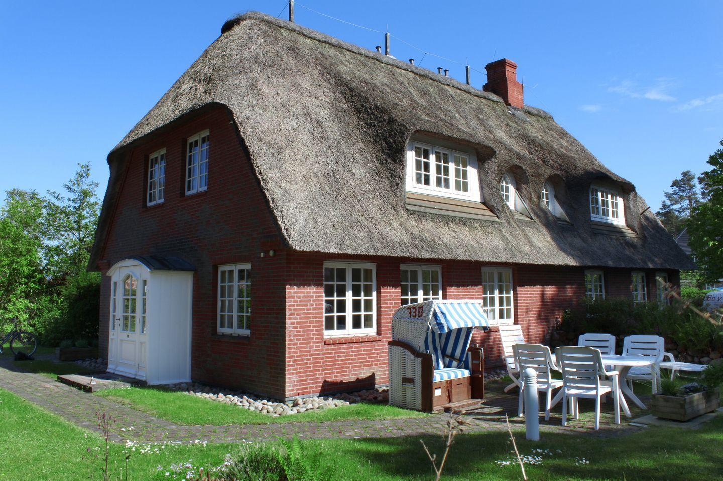 Rotes Backsteinhaus mit Strohdach, weißer Eingang und Gartenmöbel.
