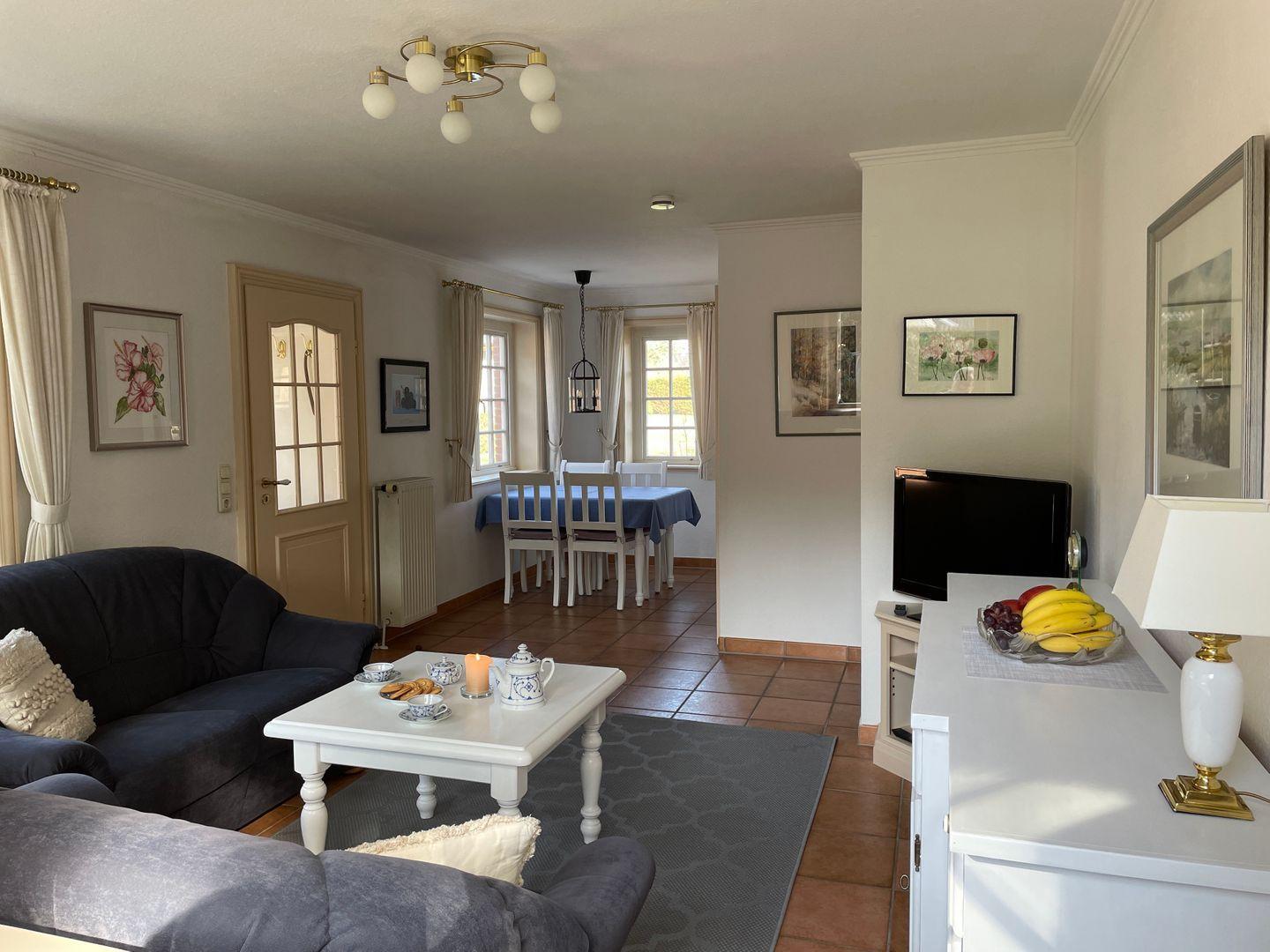 Wohn- und Essbereich mit Sofa, Tisch, Fernseher und Fenstern.