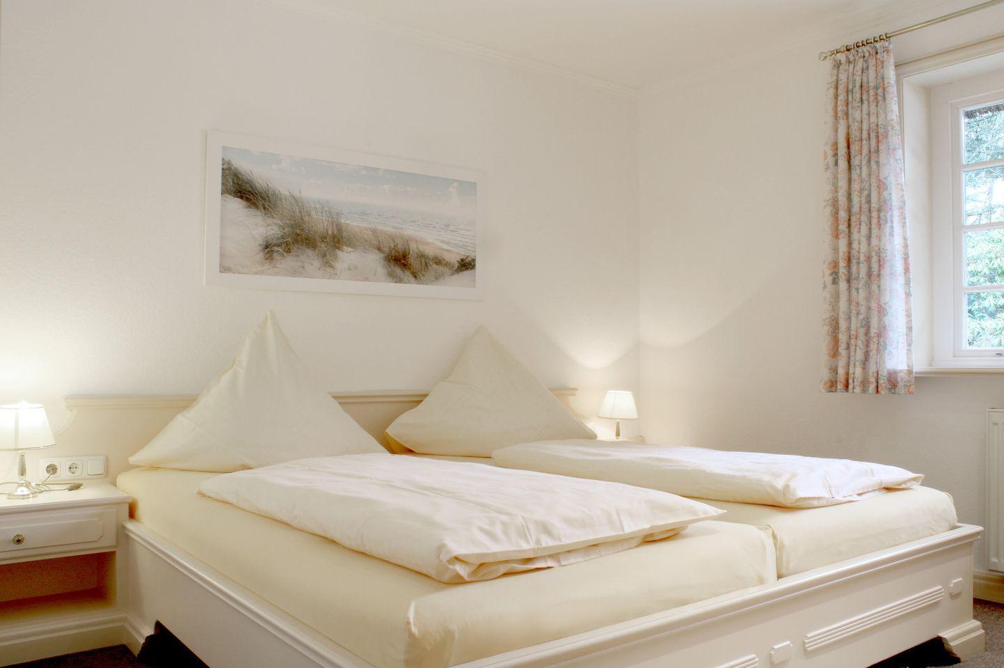 Schlafzimmer mit Doppelbett, zwei Nachttischen und Fenster mit Vorhang.