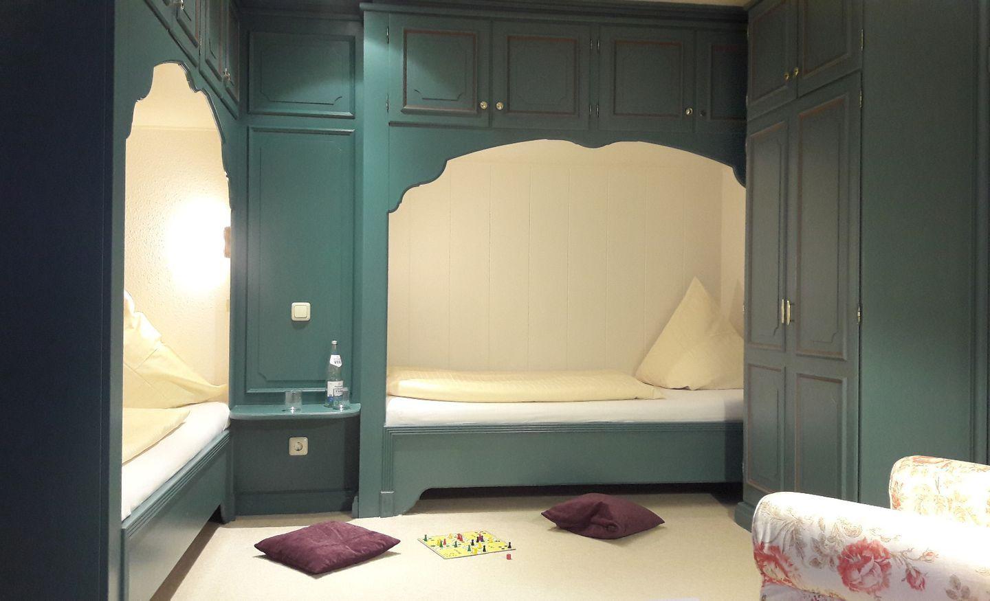 Zimmer mit zwei Betten in grünen Holzrahmen und einem Sitzbereich mit floraler Polsterung.