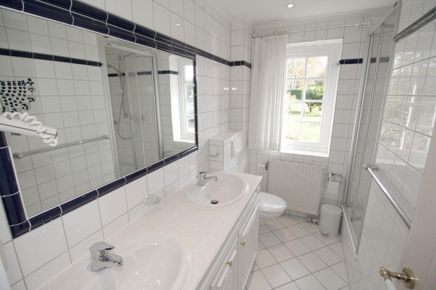 Badezimmer mit Dusche, Waschbecken und Toilette. Weiße Fliesen und Spiegel.