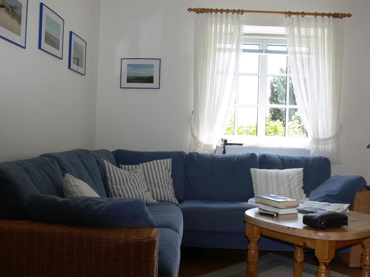 A living room with blue sofa, wooden table and window with white curtains.
