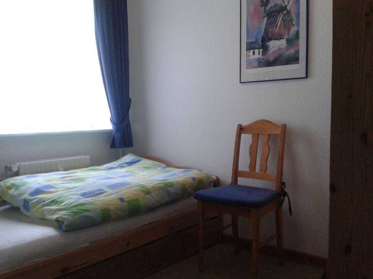 A room with a bed, a chair, and a window with a curtain.