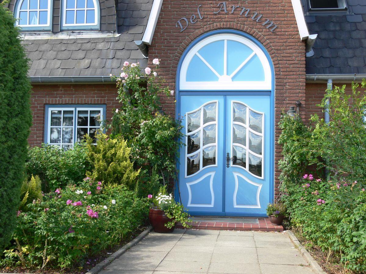 Blue entrance with arched window, surrounded by flowers and greenery.