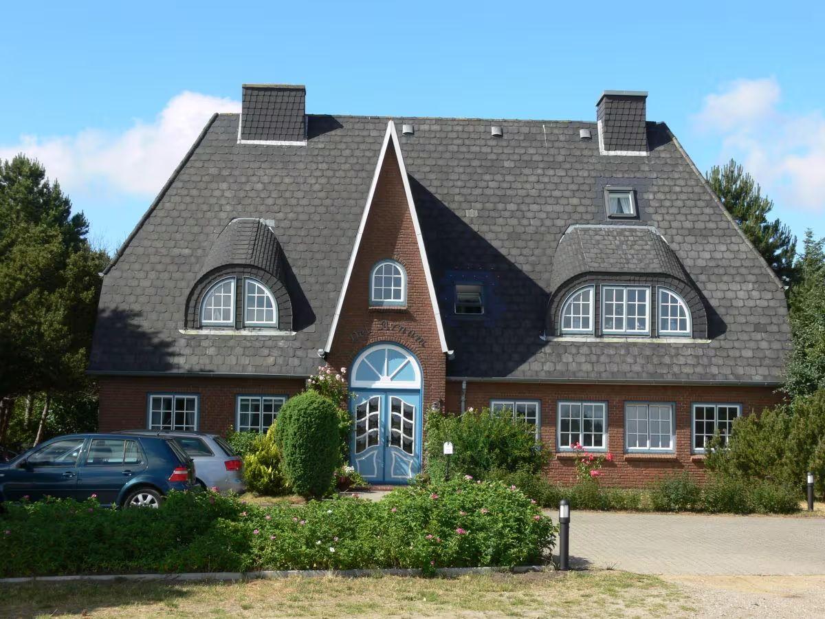A two-story house with red brick walls and a dark gabled roof. Blue door and windows are visible.