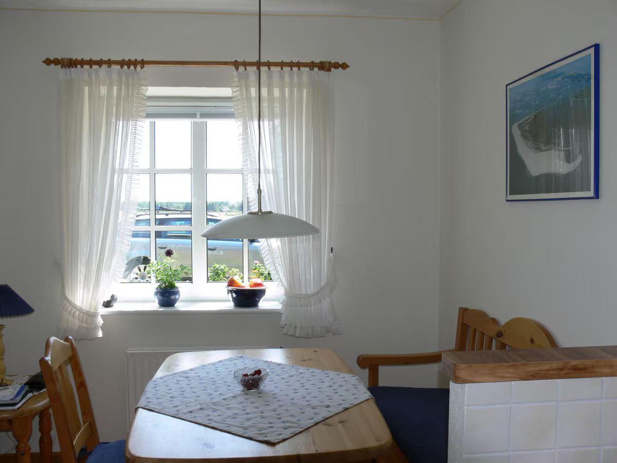 Dining room with wooden table, chairs, and window with white curtains.