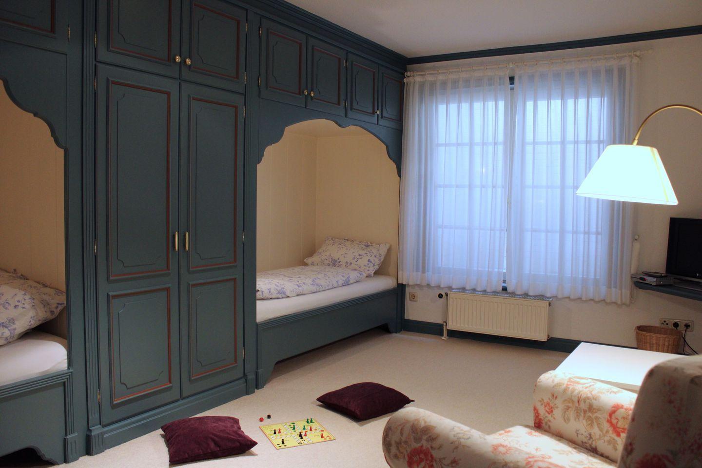 Zimmer mit integrierten Betten, Schränken und Fenster mit Vorhängen.