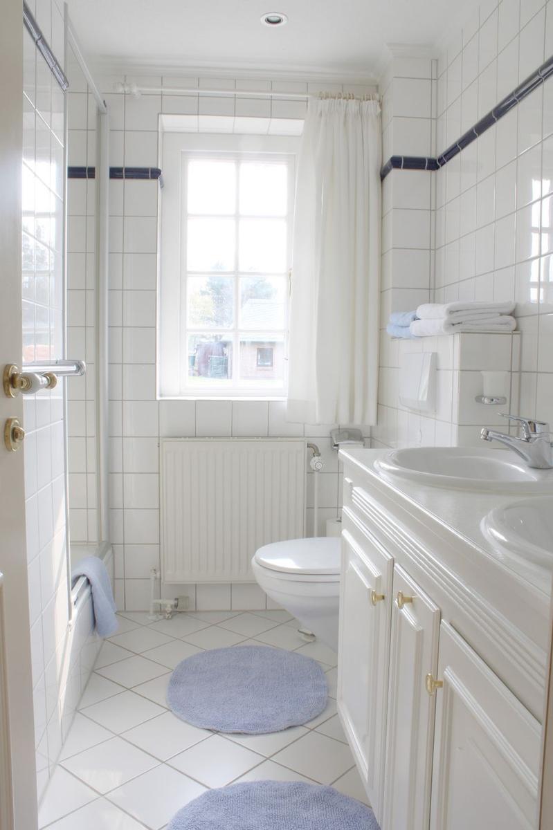 Badezimmer mit Dusche, Toilette, Waschbecken und Fenster mit Vorhang.