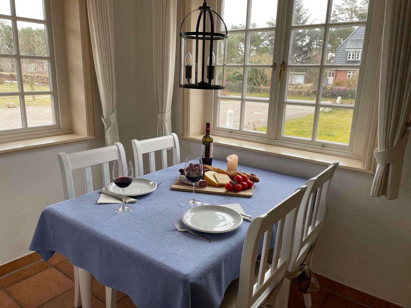 Esstisch mit blauer Tischdecke, weißen Stühlen und Blick auf Garten.