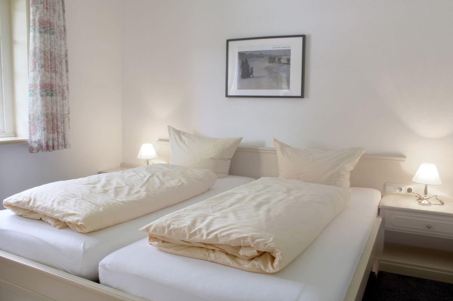 Zwei Einzelbetten mit Bettwäsche, Nachttische und Lampe, Wandbild und Fenster mit Vorhang.