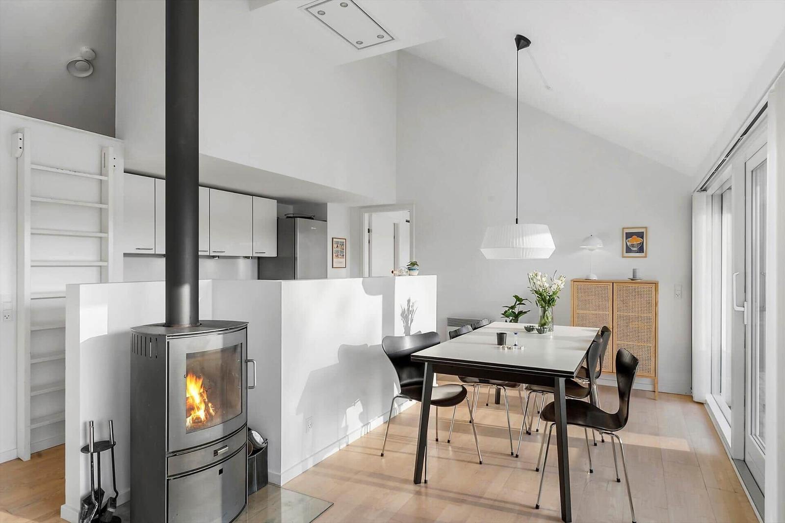 Dining area with table, chairs, and wood stove. Background: kitchen and glass doors.