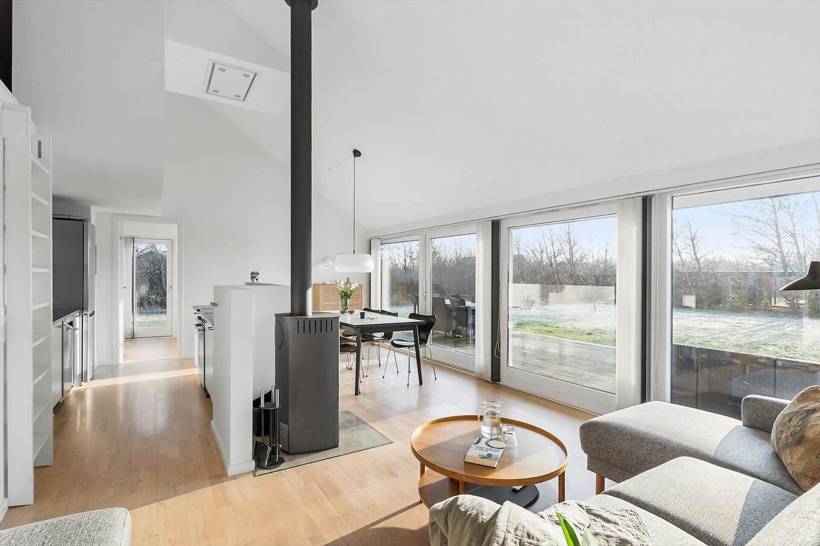 Living and dining area with wooden floor, large windows, and wood stove.