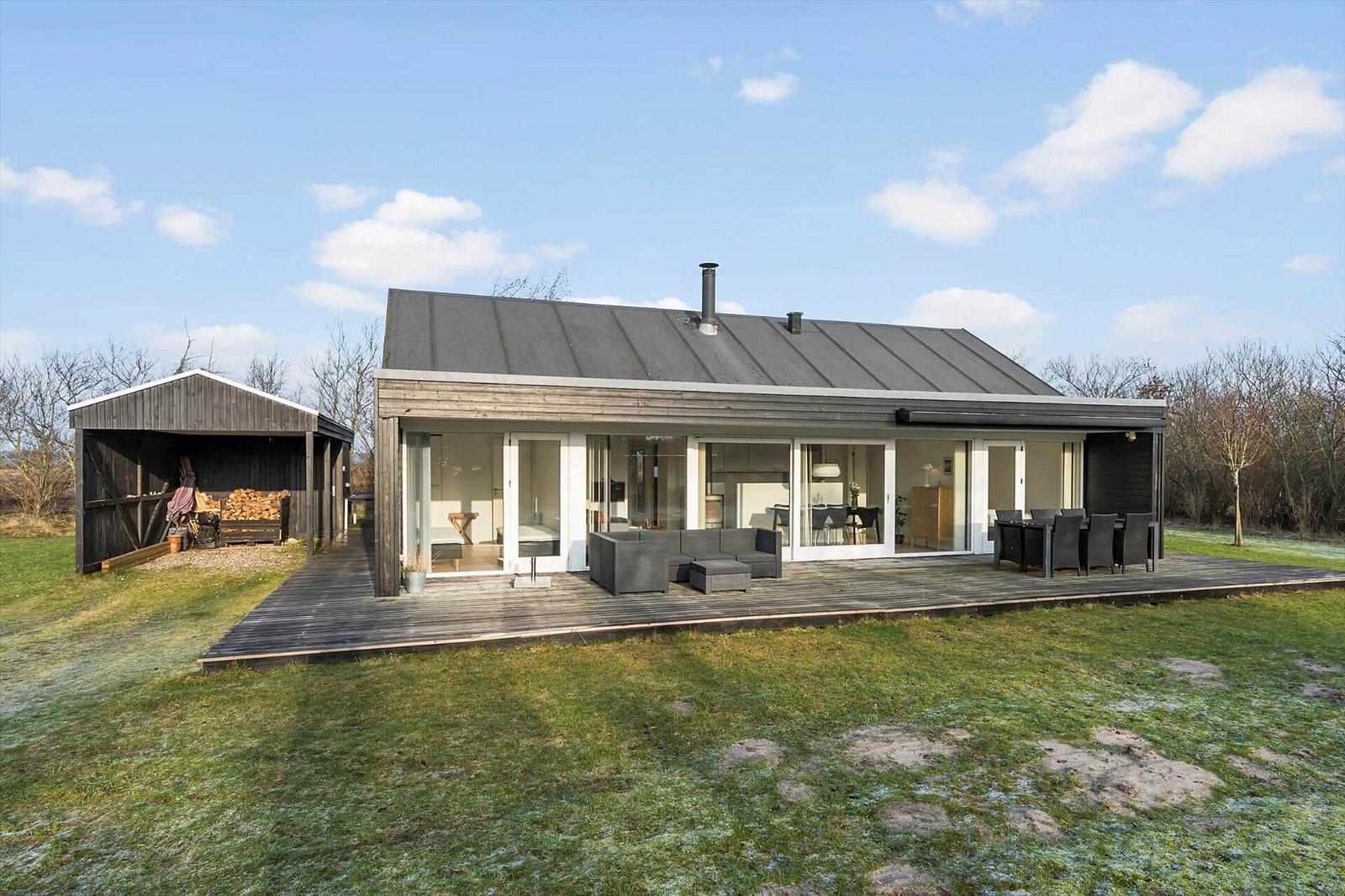 Modern villa with large wooden deck, seating, and view of the garden.