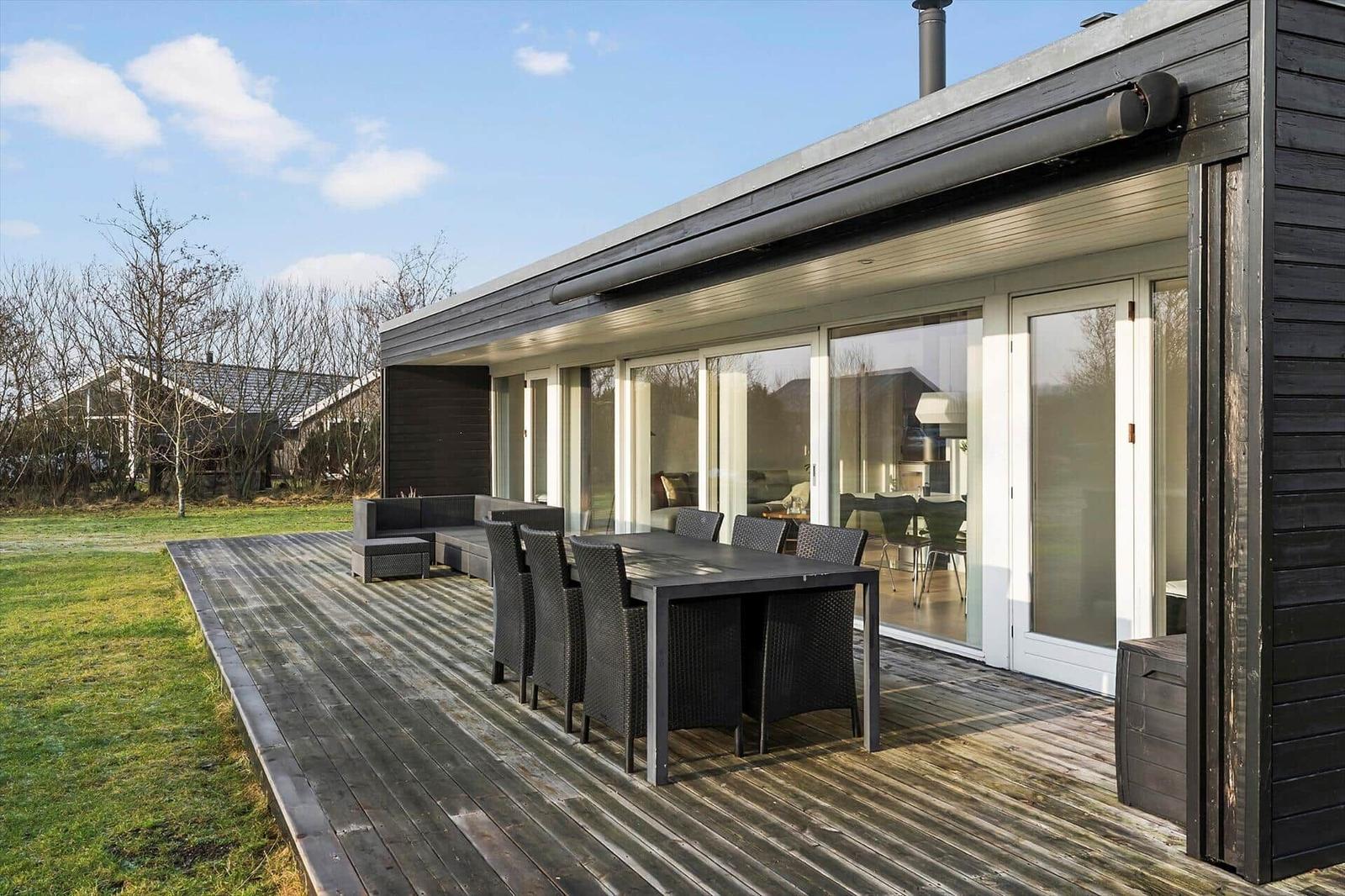 Deck with table, chairs, and sofa. Glass doors lead to interior.
