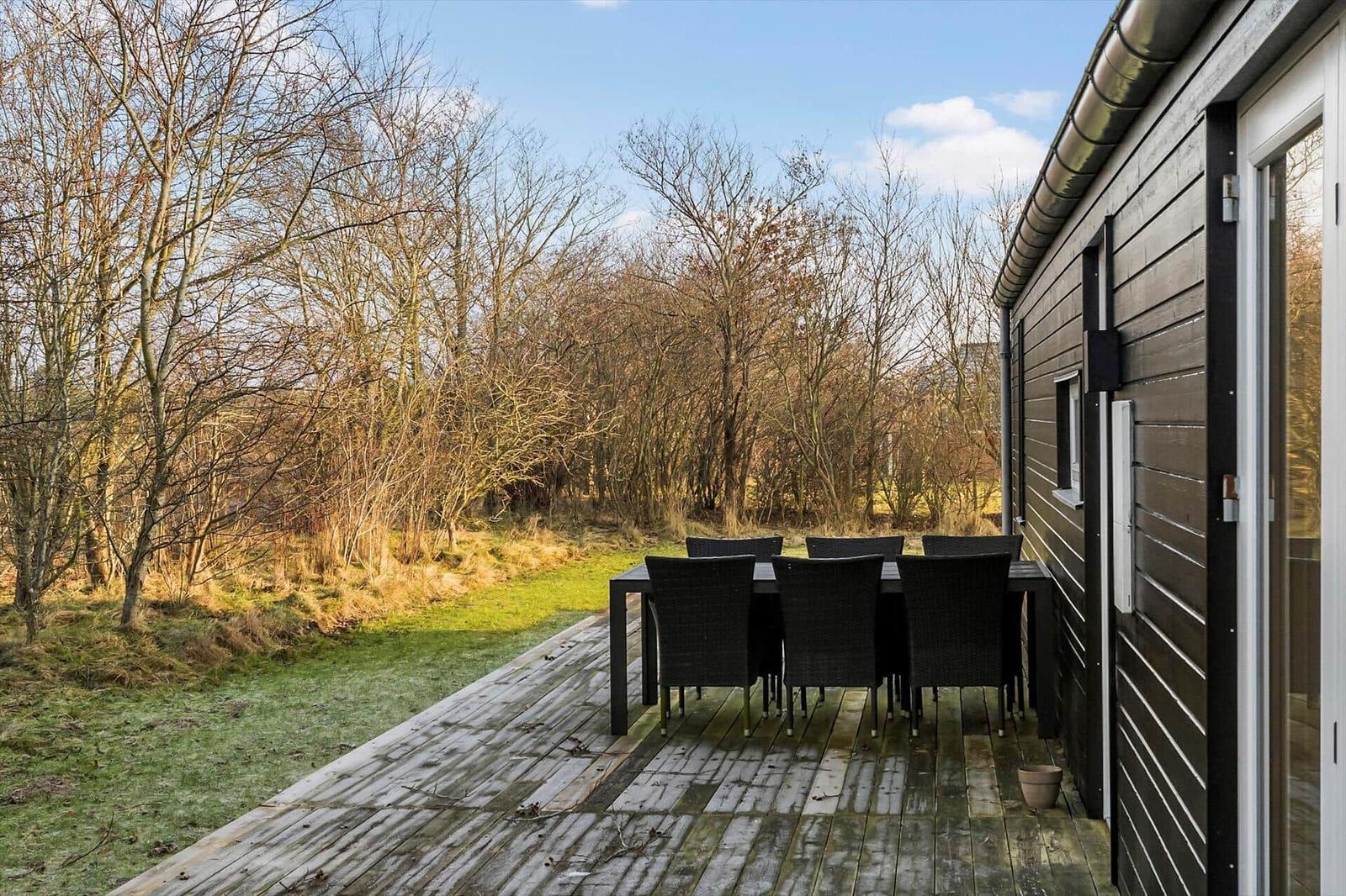 Deck with table and chairs next to a house with wooden siding.