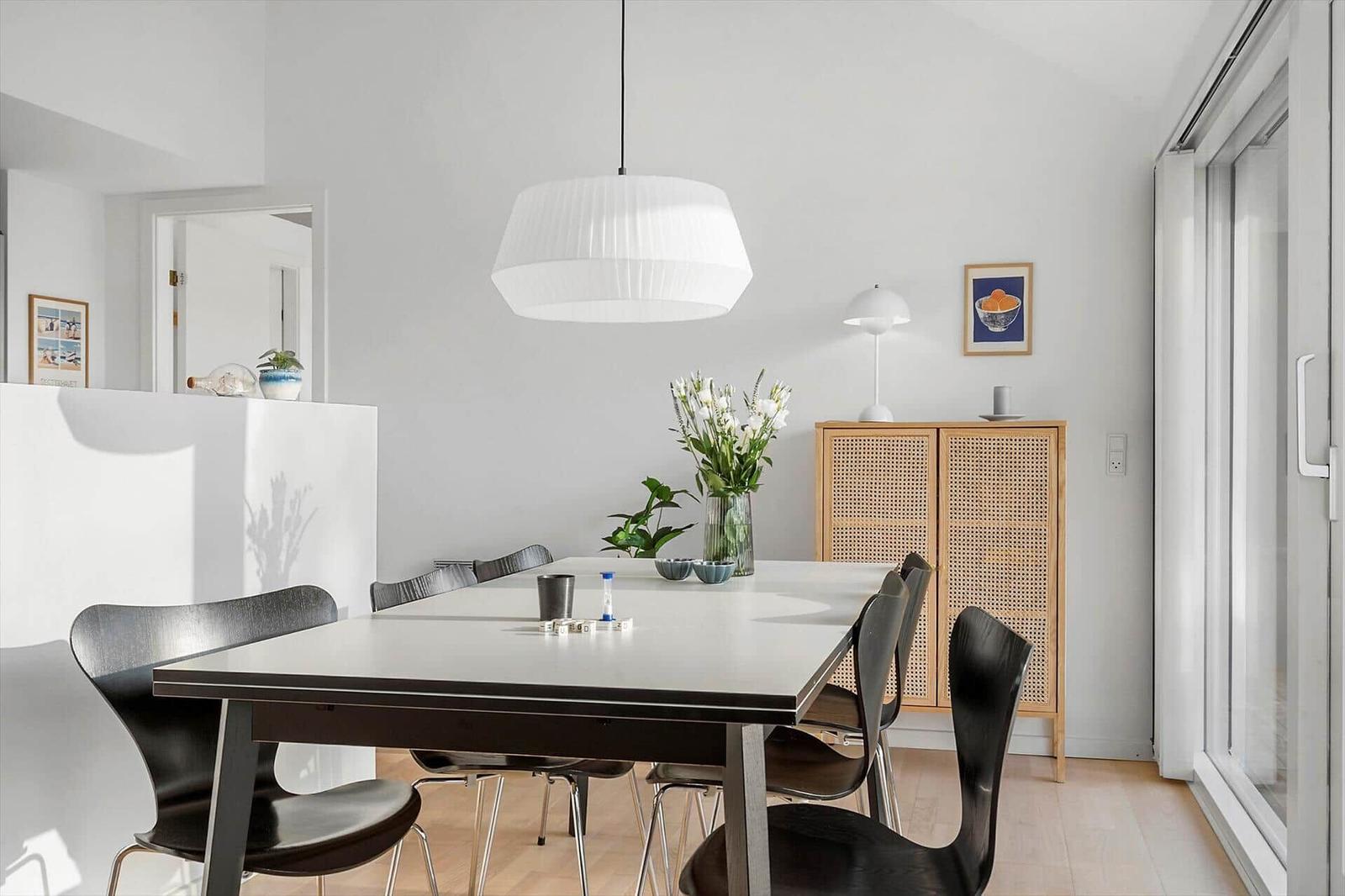 Dining room with table, chairs, and lighting. Background: cabinet and window.