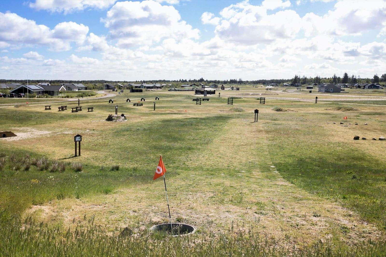 Golf course with bunkers and picnic tables under blue sky.