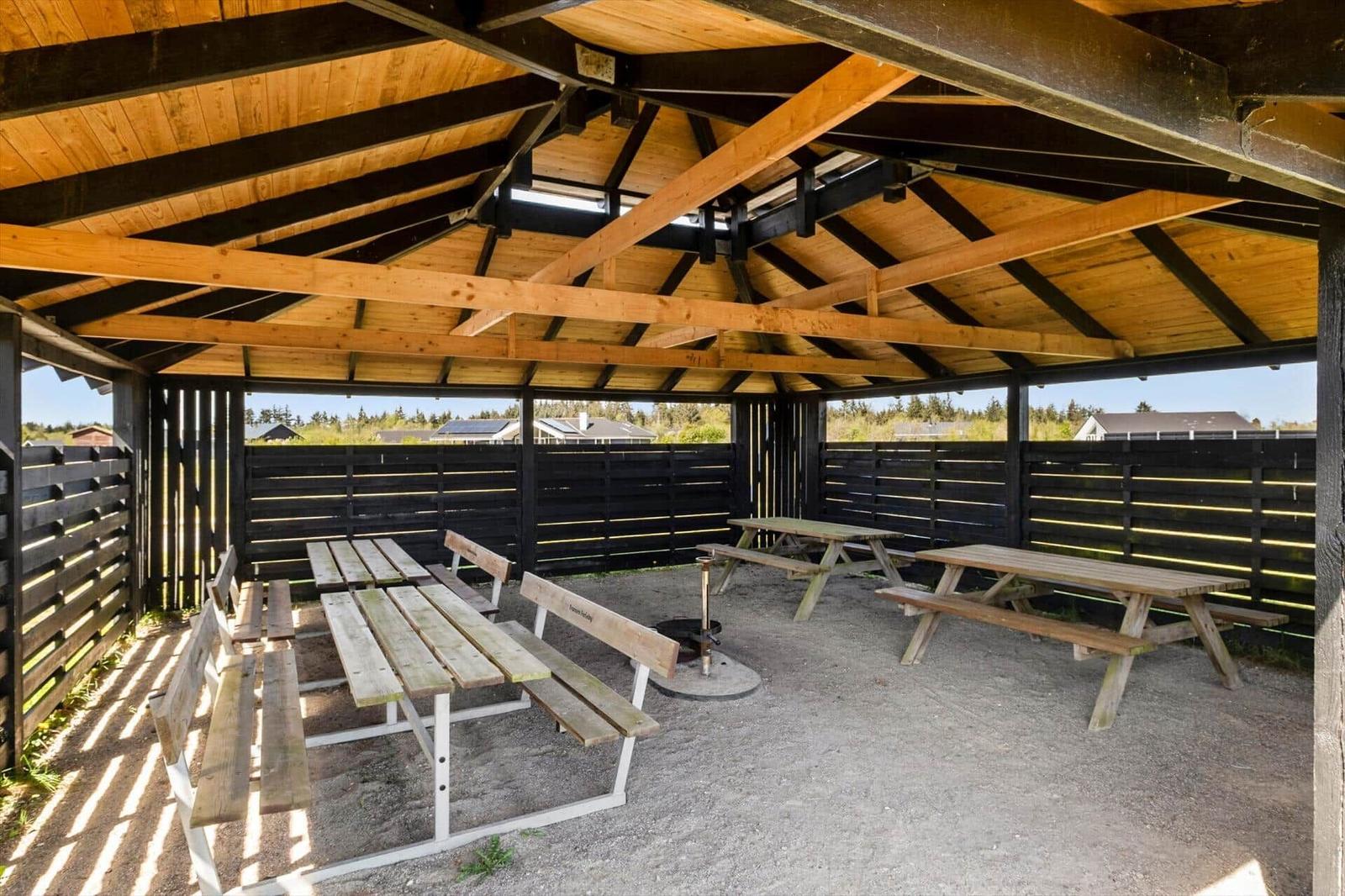 Shingled roof over wooden benches and grill area with view of houses.