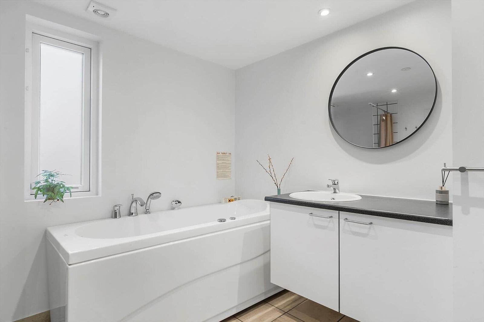 Bath with whirlpool, sink, and round mirror. Window with plant.