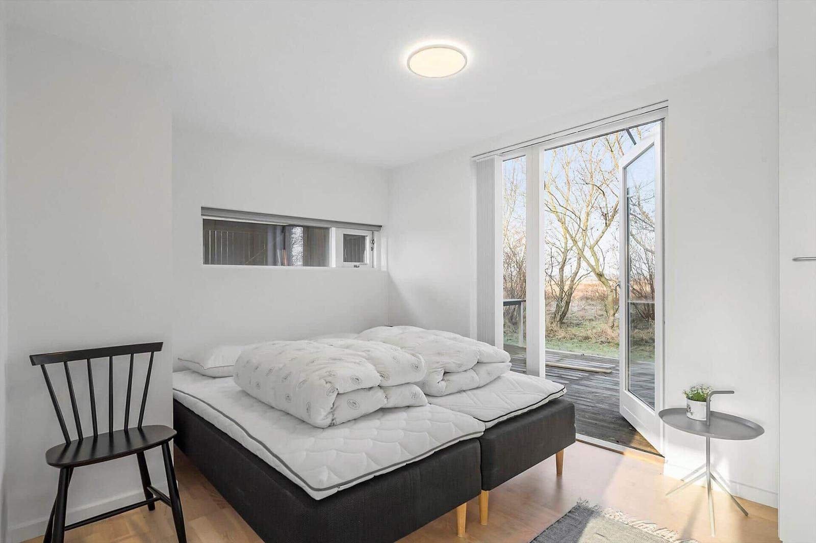 Bedroom with double bed, chair, and balcony door. Trees are visible outside.