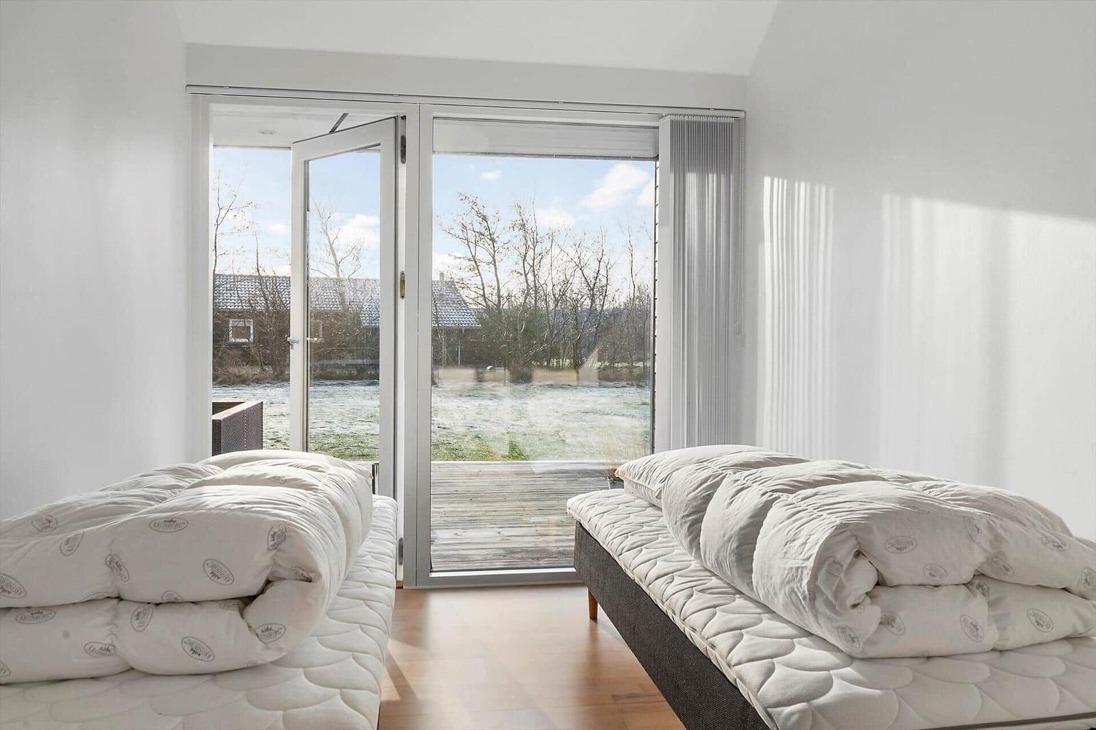 Two beds with duvets in a room with view of a terrace and landscape.
