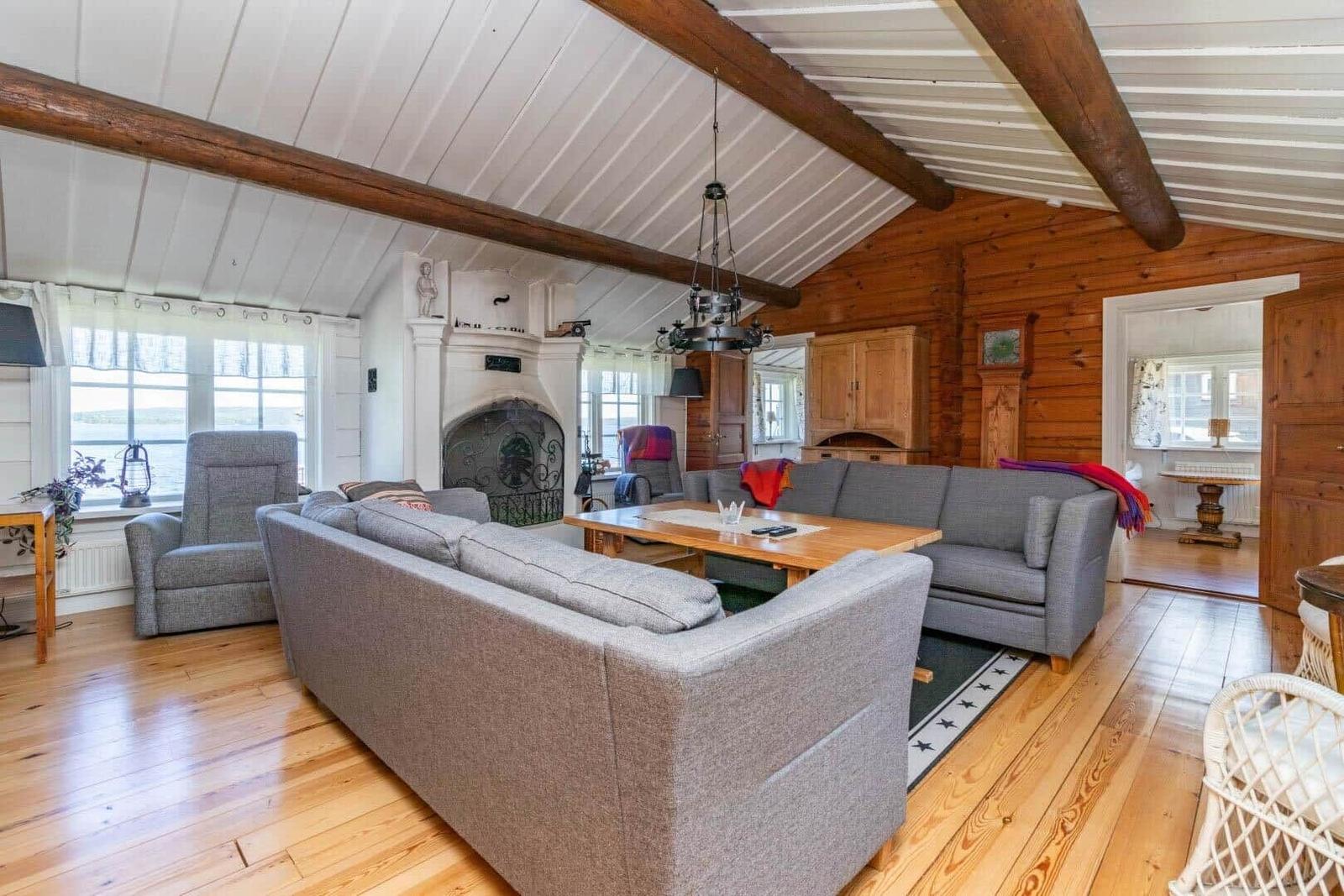 Wohnzimmer mit Holzboden, grauen Sofas und Kamin. Holzdecke mit Balken.