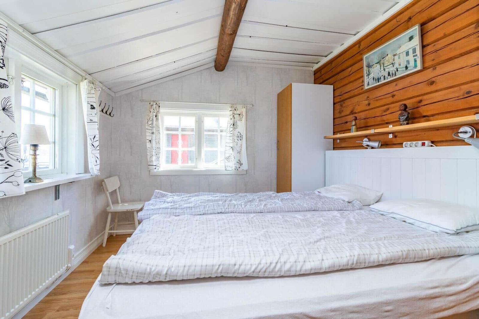 Schlafzimmer mit Bett, Fenstern, Kleiderständer und Holzwand.