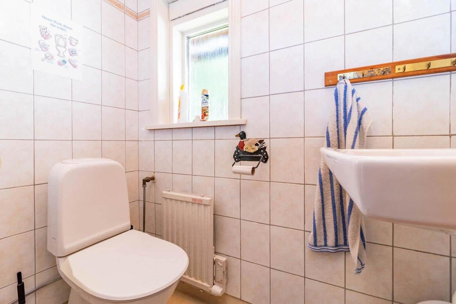 Badezimmer mit Toilette, Waschbecken und Fenster. Handtuch hängt an Wandhalter.