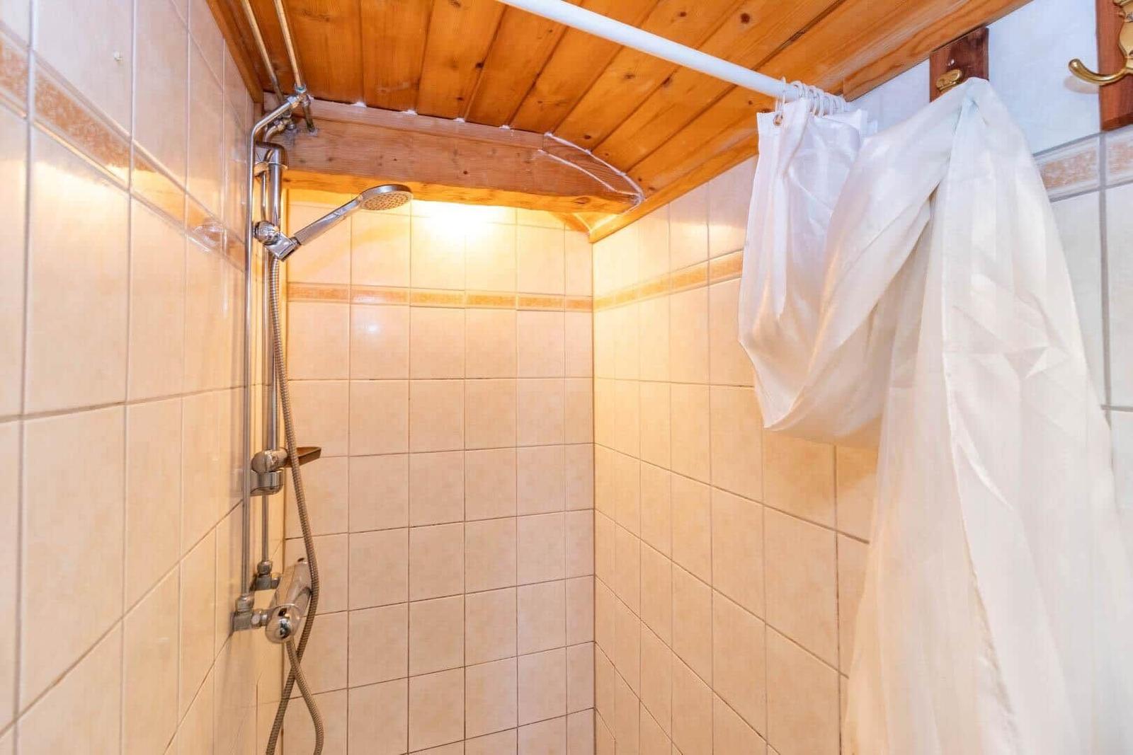 Dusche mit Duschbrause und weißen Vorhängen an Holzdecke.