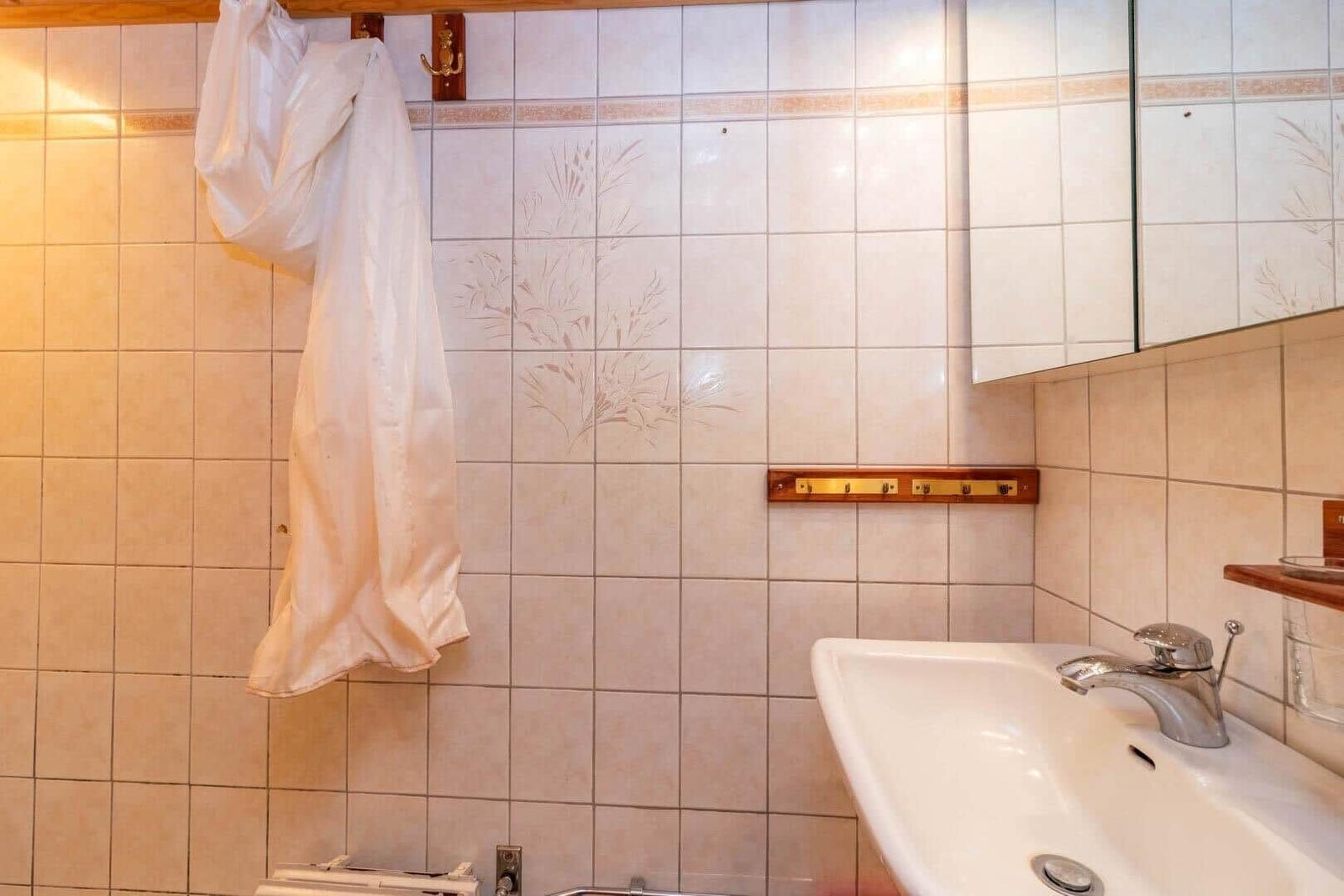 Bad mit Waschbecken, Spiegel und weißen Fliesen.