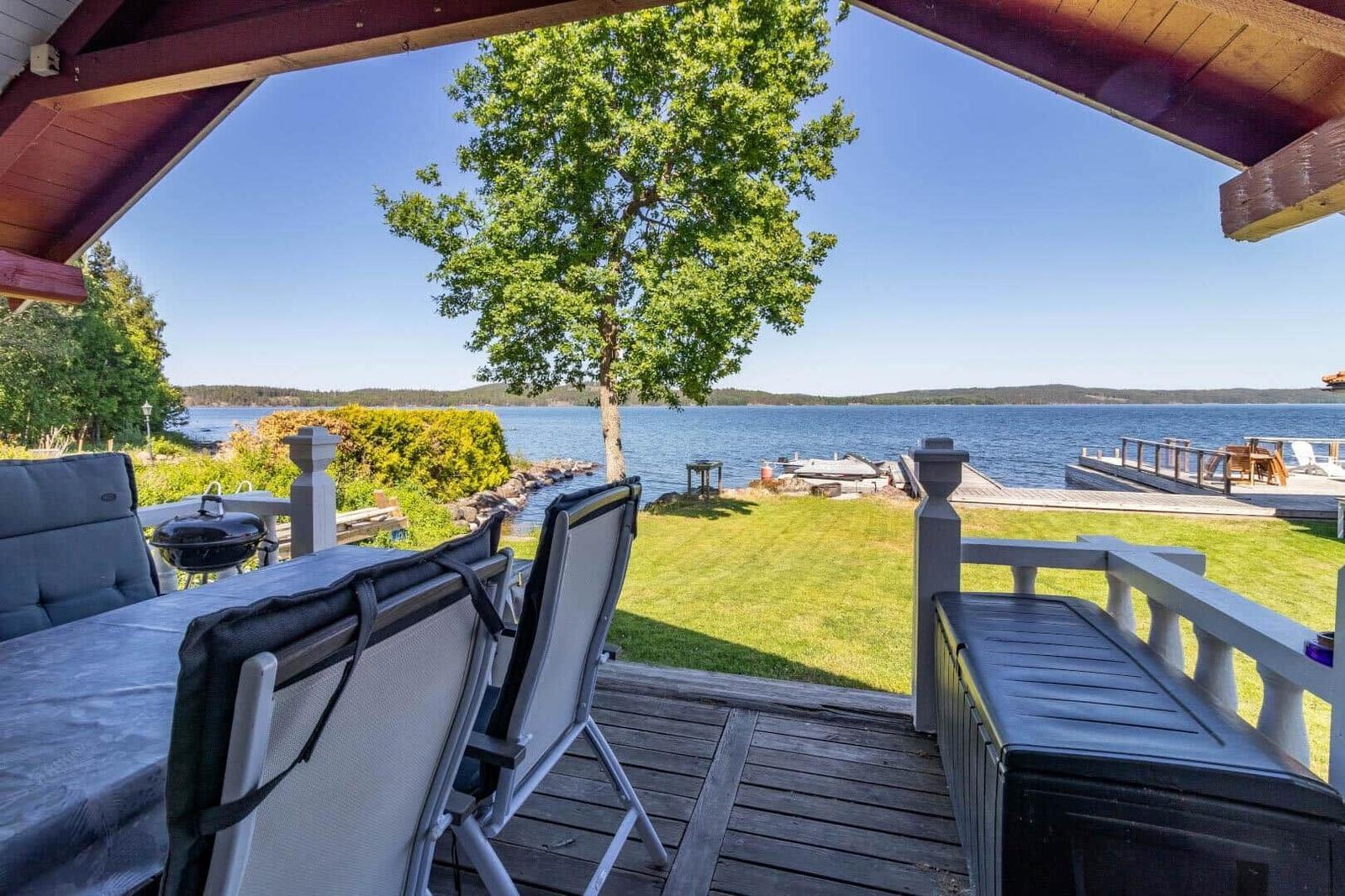 Terrasse mit Gartenmöbeln und Blick auf See und Holzsteg.