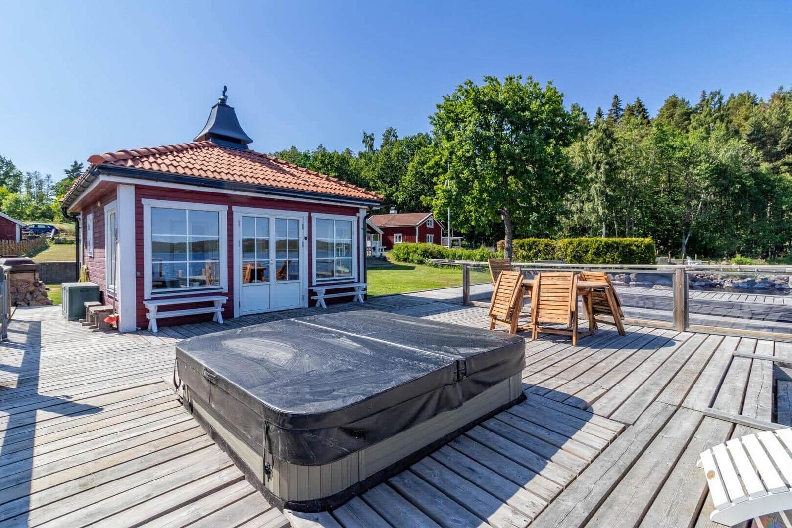 Rotes Haus mit Terrasse, Whirlpool und Holzmöbeln am Wasser.