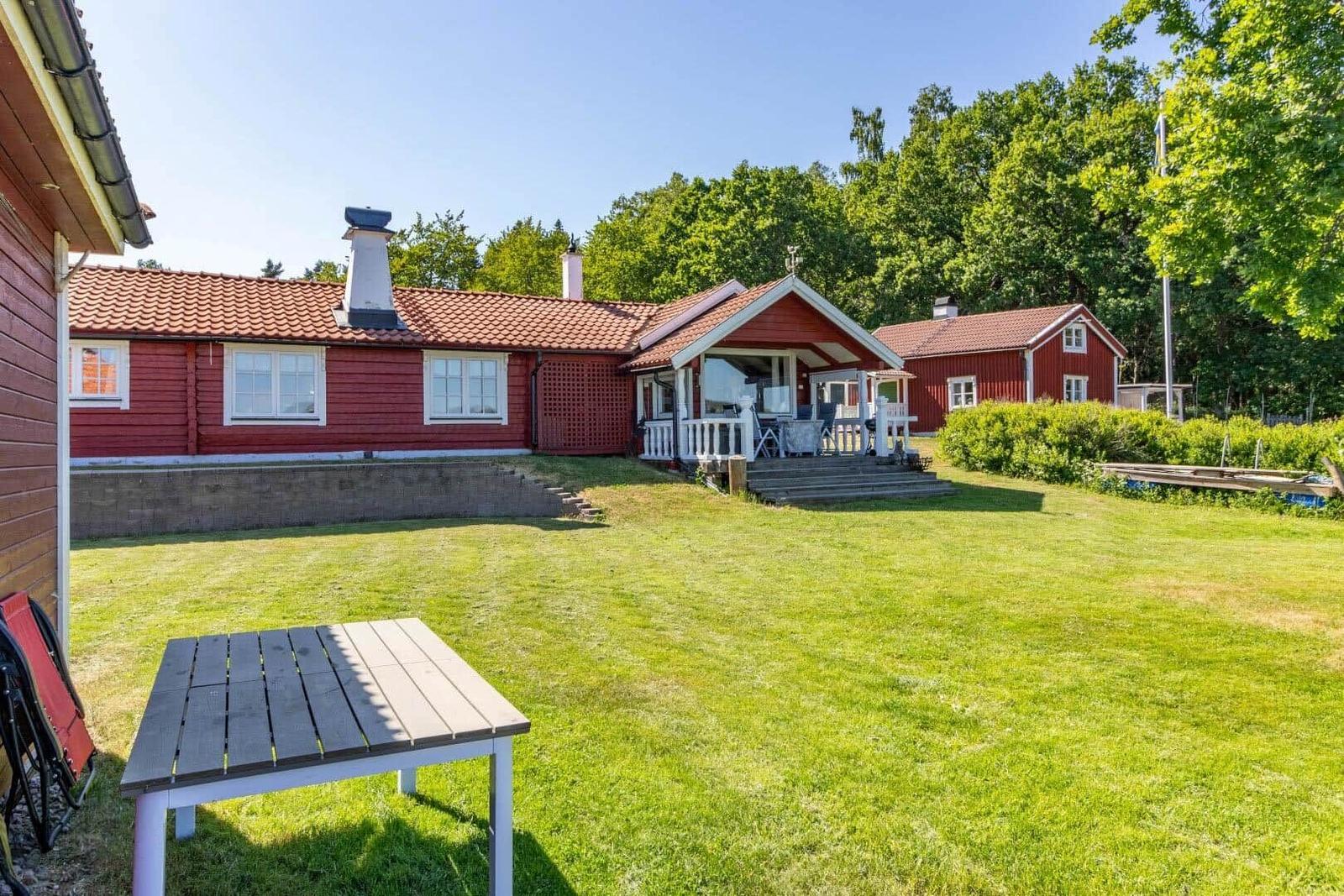 Roter Holzhaus mit Terrasse und großem Garten. Tisch und Stühle im Vordergrund.