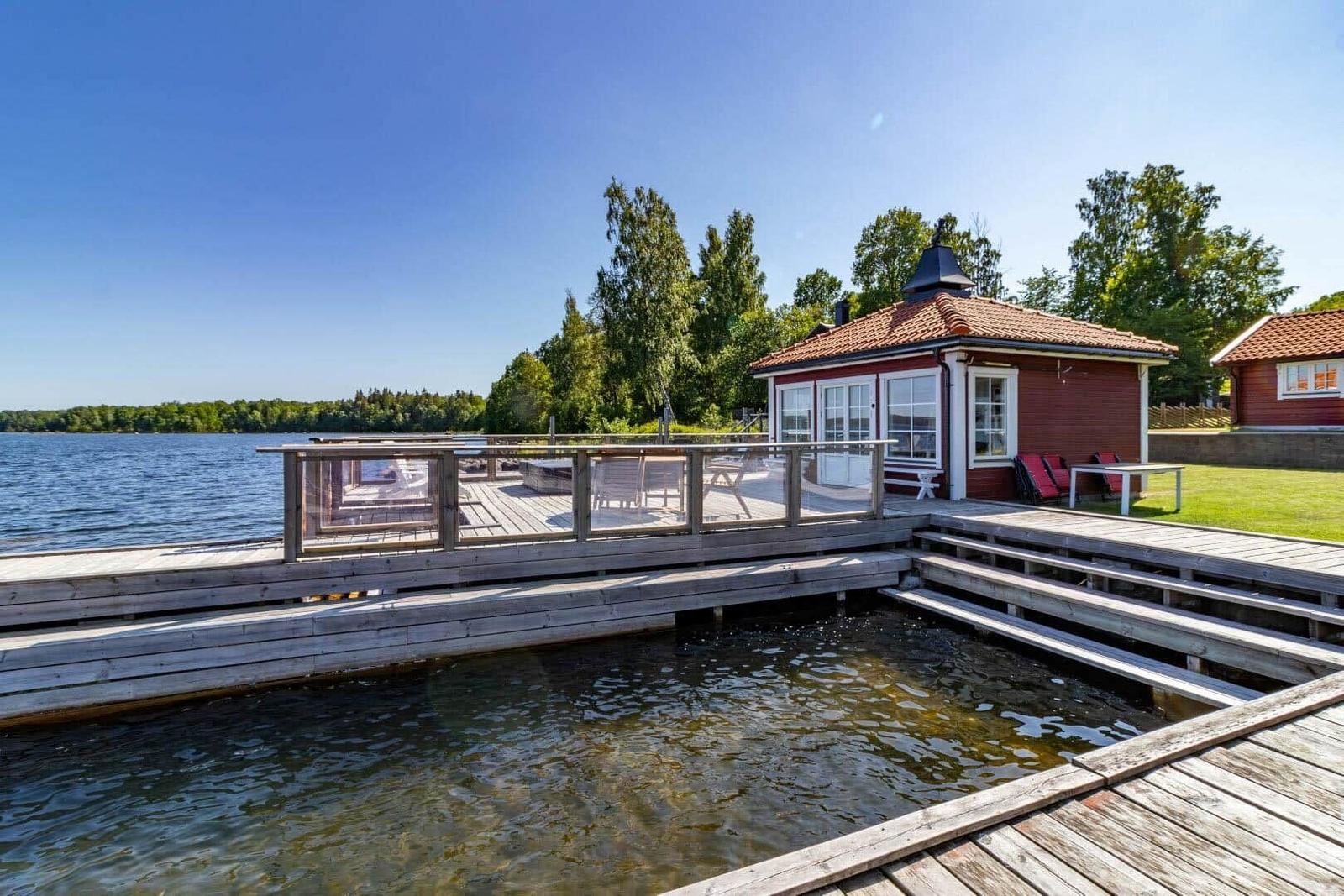 Rotes Holzhaus am Wasser mit Terrasse und Liegeflächen.