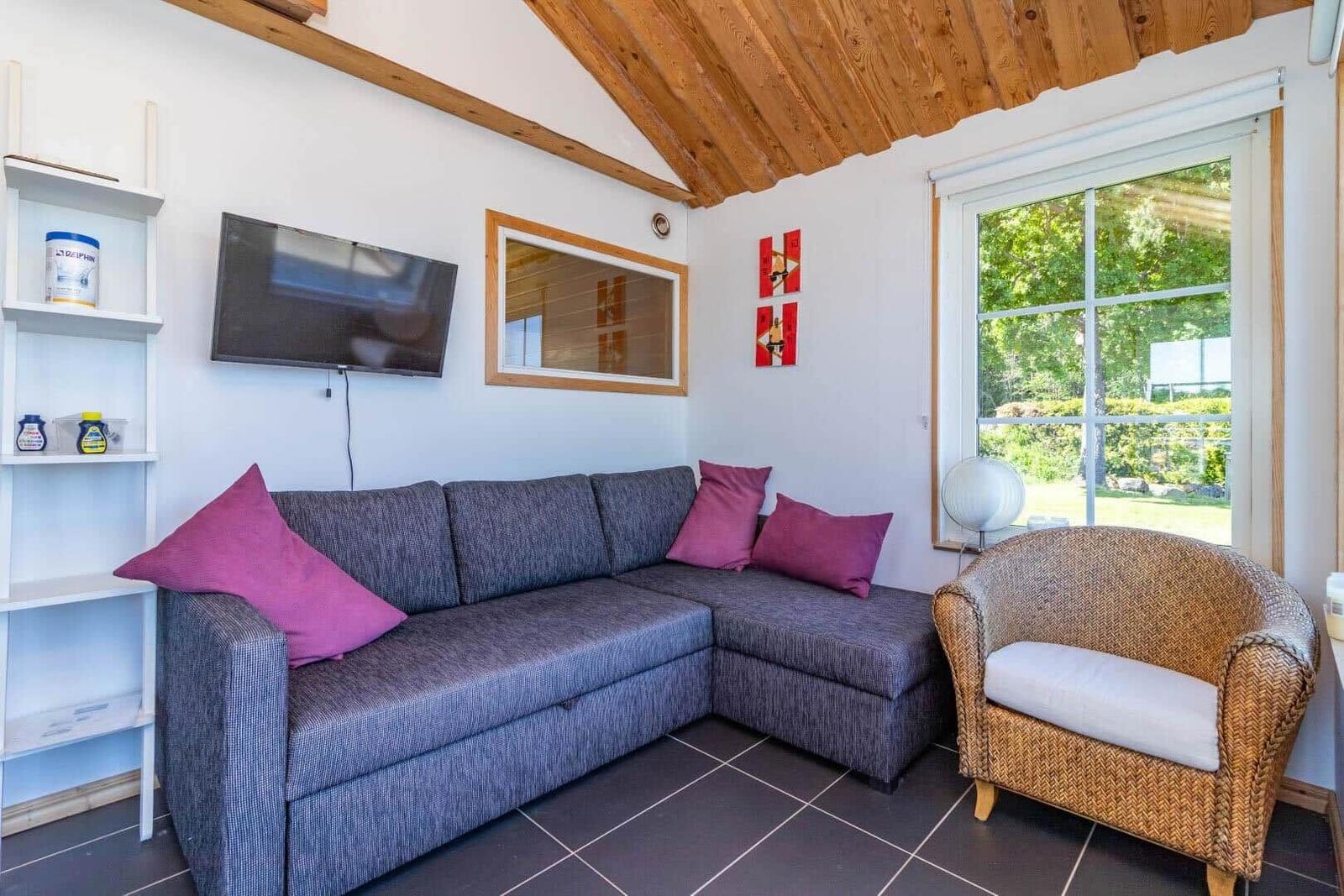 Ein Wohnzimmer mit grauem Sofa, purpurfarbenen Kissen und einem geflochtenen Sessel.