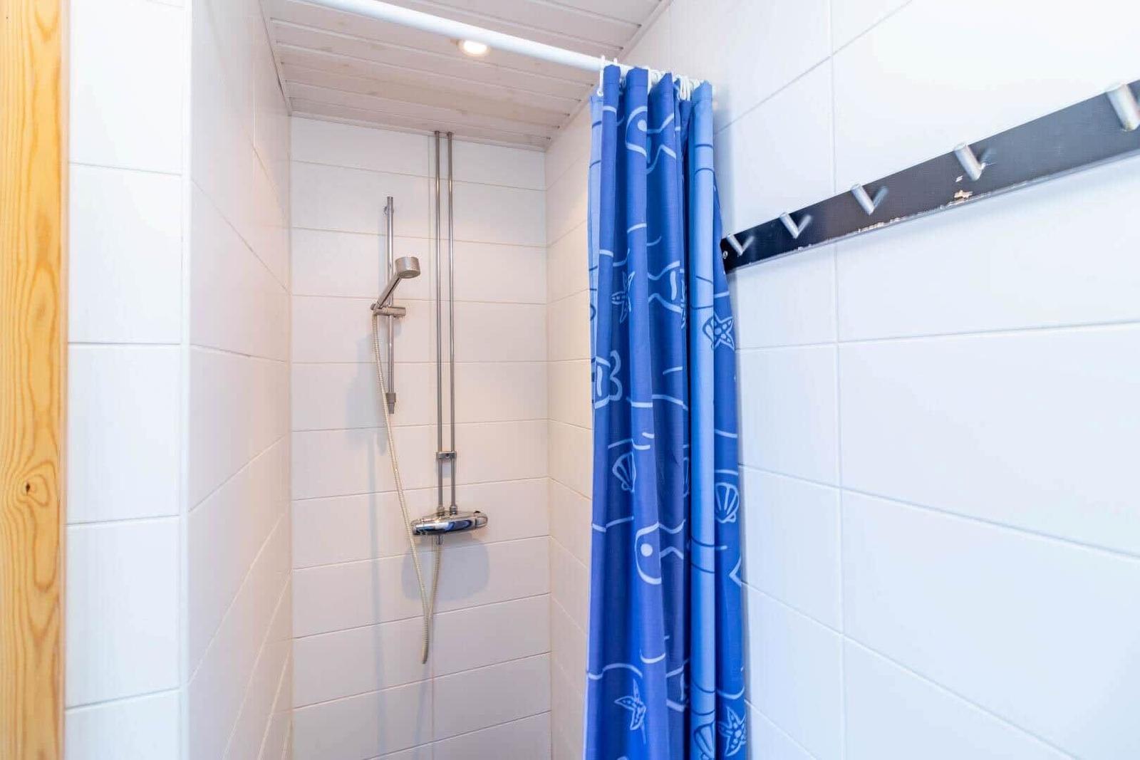 Dusche mit blauem Vorhang und silberner Duschkopf an weißen Fliesen.