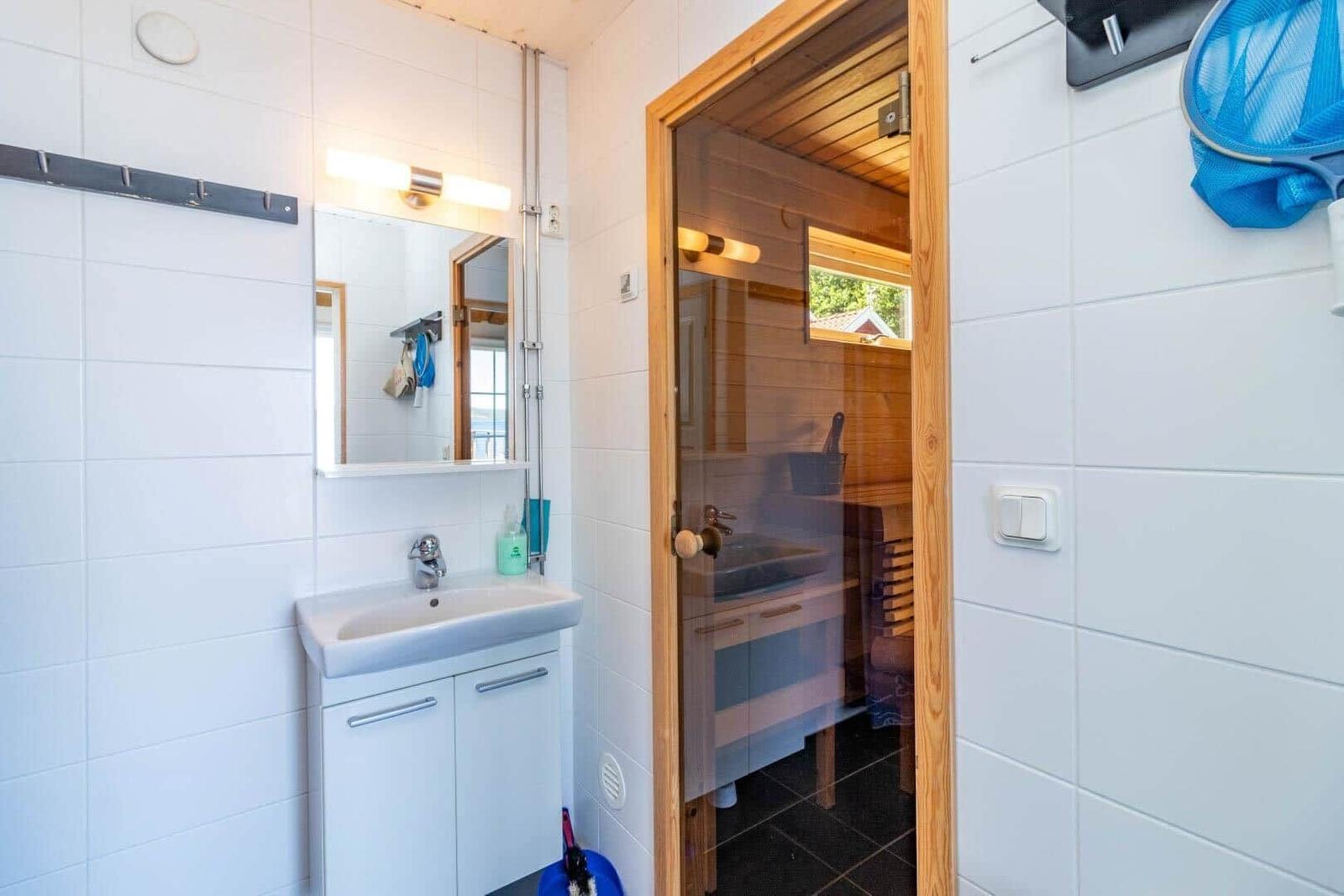 Badezimmer mit Waschbecken und Dusche. Sauna im Hintergrund mit Holzwand.