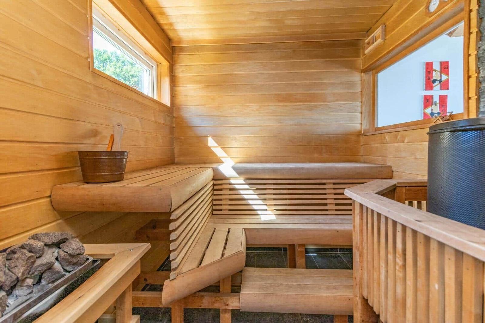 Holzsauna mit Sitzbänken, Fenstern und Steinen.