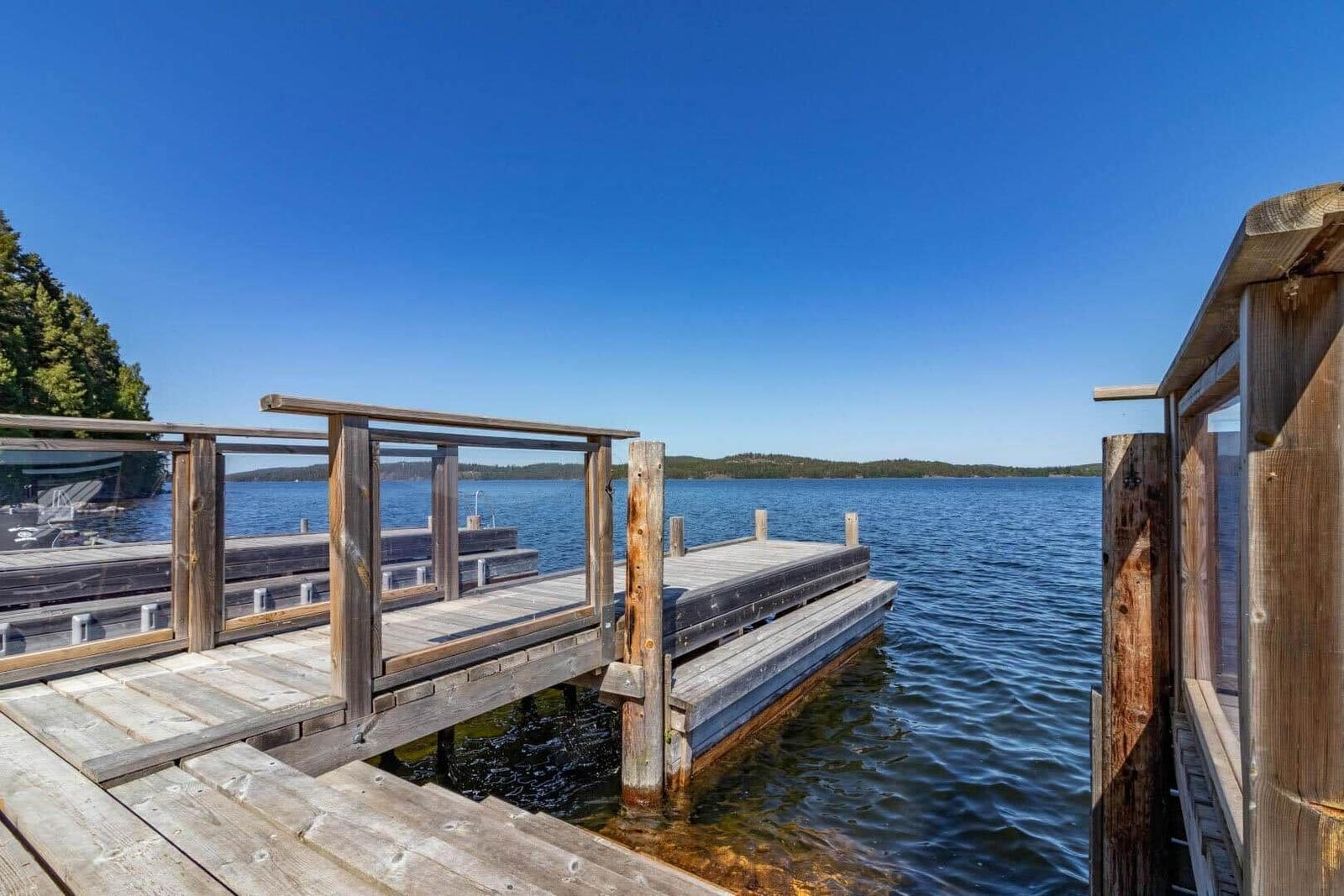 Holzsteg führt zum Wasser. Boot liegt am Ufer. Himmel klar und blau.