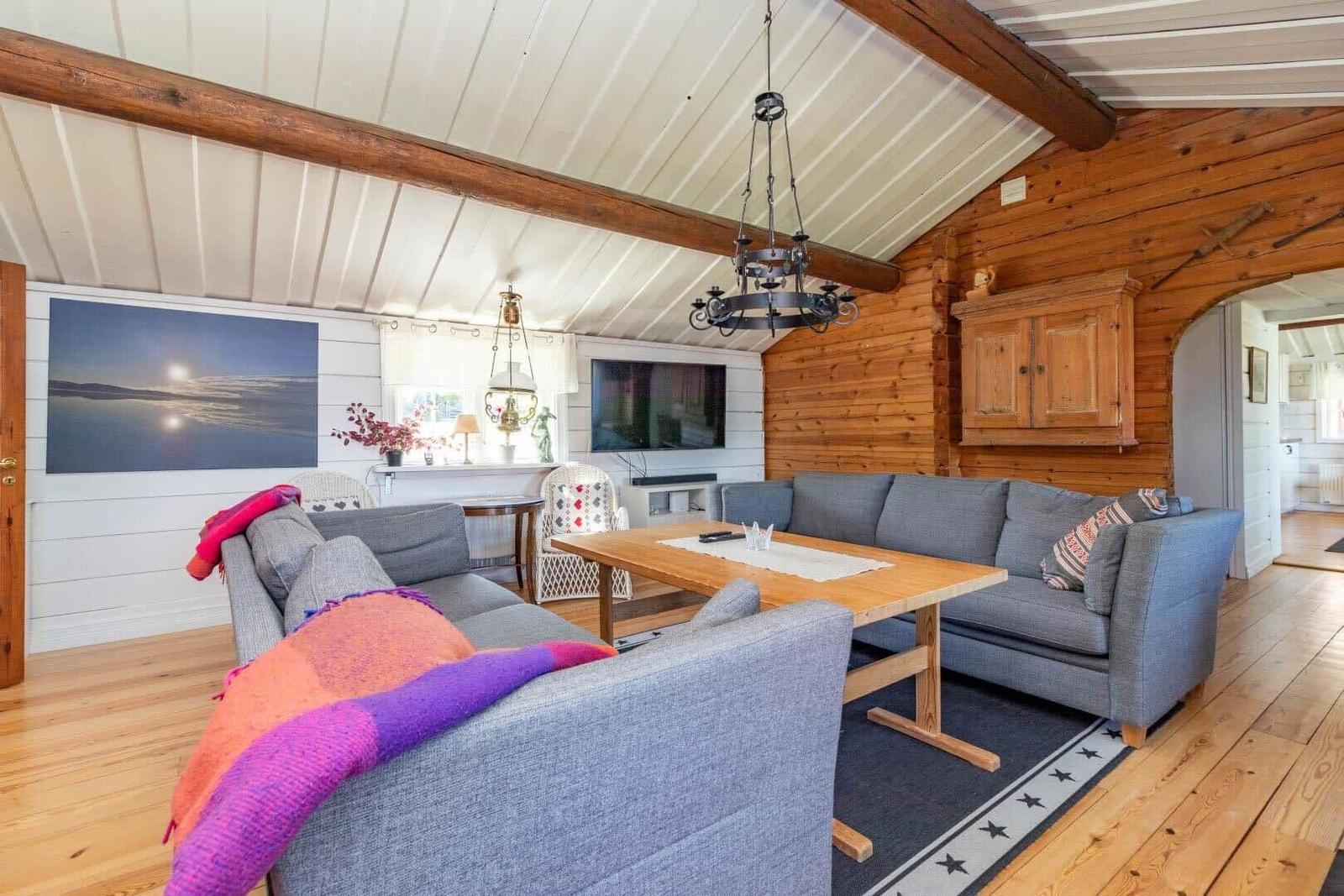 Wohnzimmer mit grauem Sofa, Holztisch und Holzwand. Fernseher und Wandbild sind sichtbar.