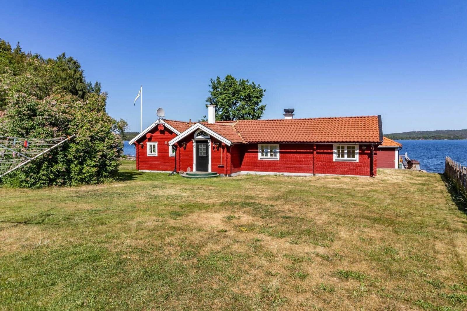 Rotes Holzhaus am See mit Garten und Schwimmbad.