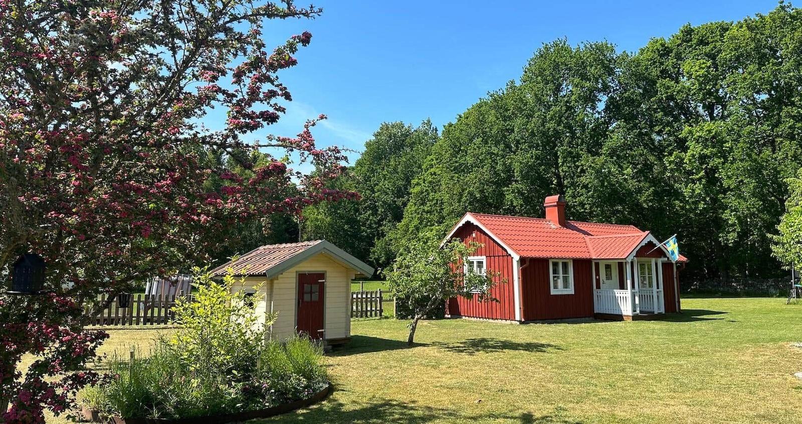 Rotes Holzhaus mit weißen Fenstern und einer Terrasse. Neben einem kleineren gelben Gebäude mit roter Tür.