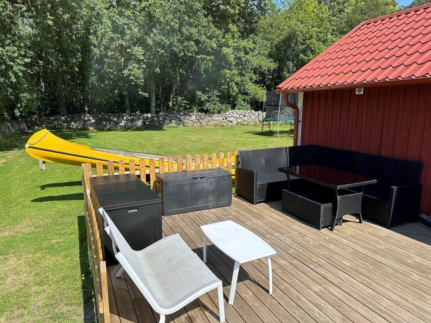 Terrasse mit Gartenmöbeln, gelbem Kanu und rotem Holzhaus mit Dach.