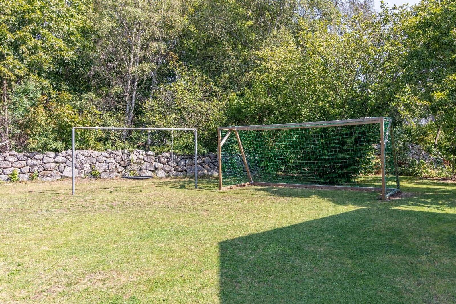 Grüner Rasenplatz mit zwei Fußballtoren und Steinmauer im Hintergrund.
