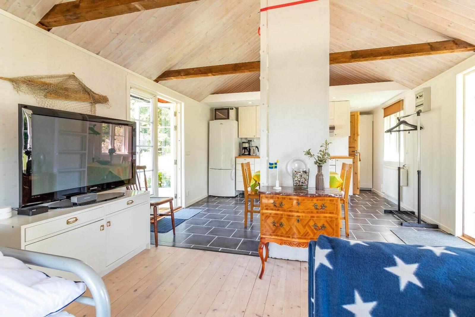 Wohnbereich mit TV, Essbereich und Küche unter Holzdecke.