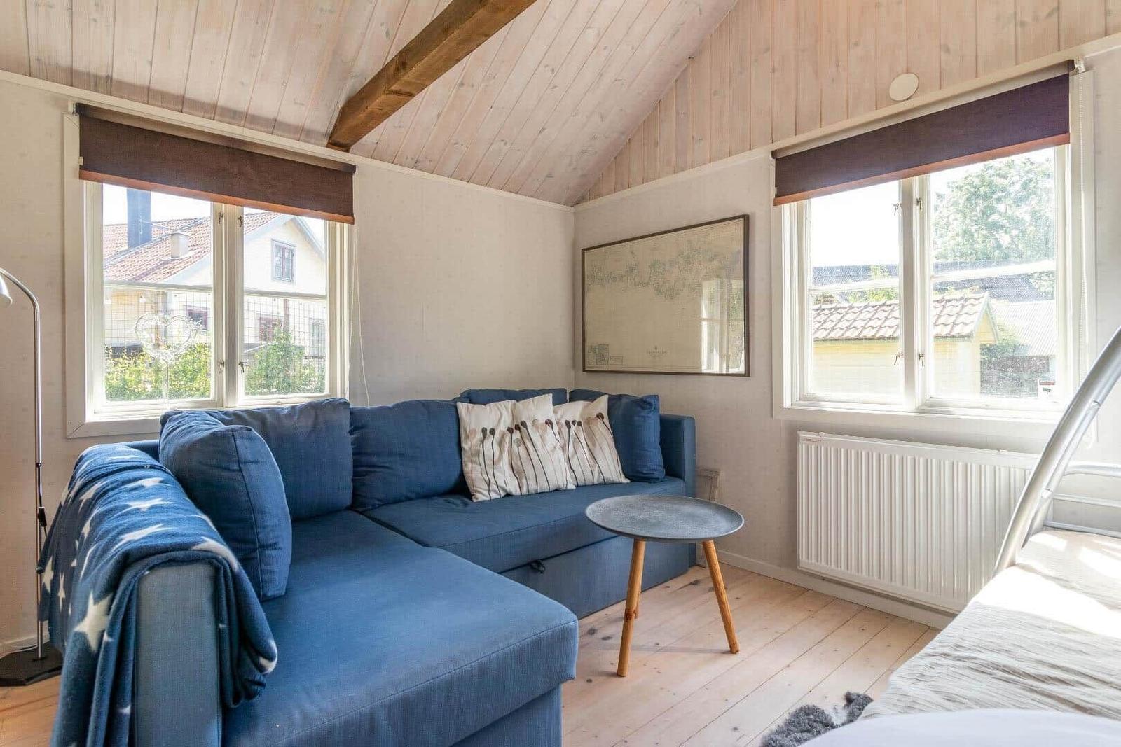 Ein Wohnzimmer mit blauem Sofa, Holzboden und zwei Fenstern mit Blick auf Häuser.