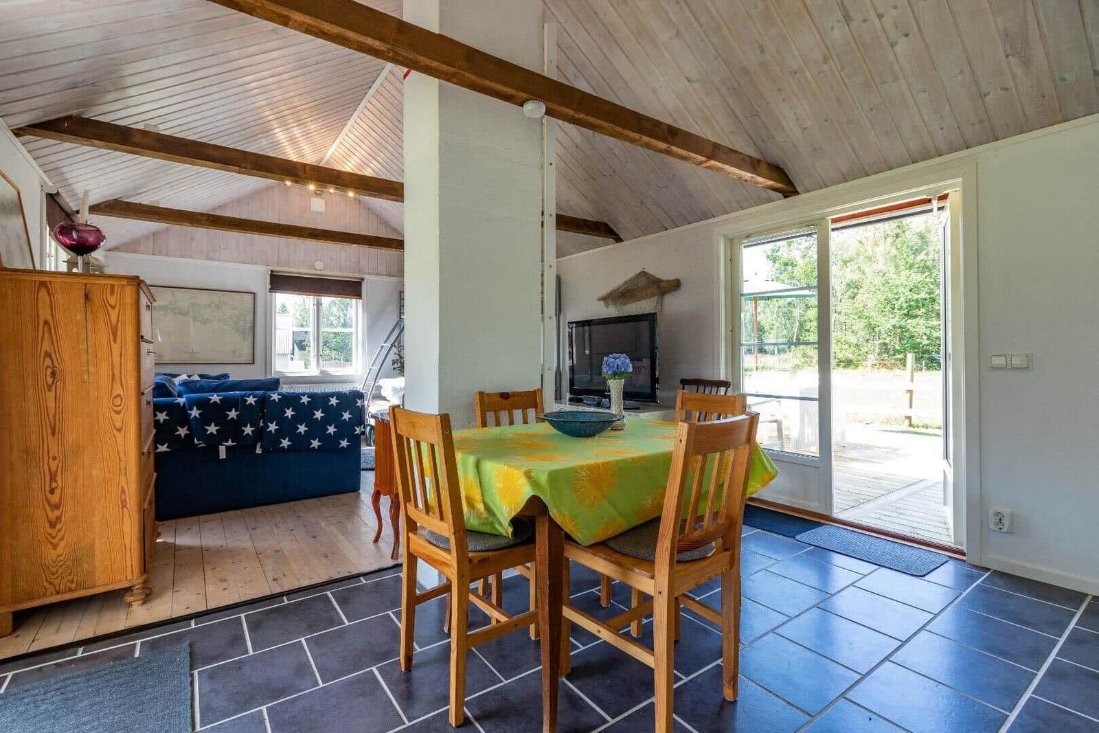 Essbereich mit Holztisch und Stühlen, dahinter Wohnbereich mit Sofa und Fernseher.