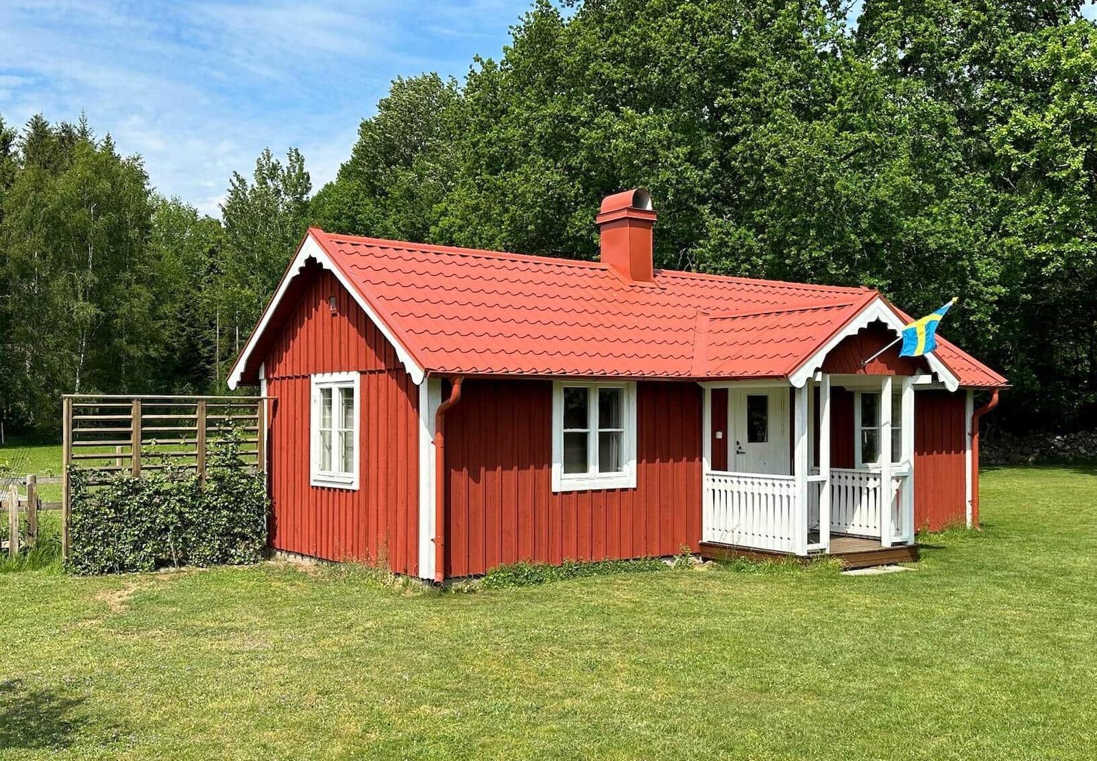 Rotes Holzhaus mit weißen Fensterrahmen und Veranda. Schwedische Flagge weht im Wind.