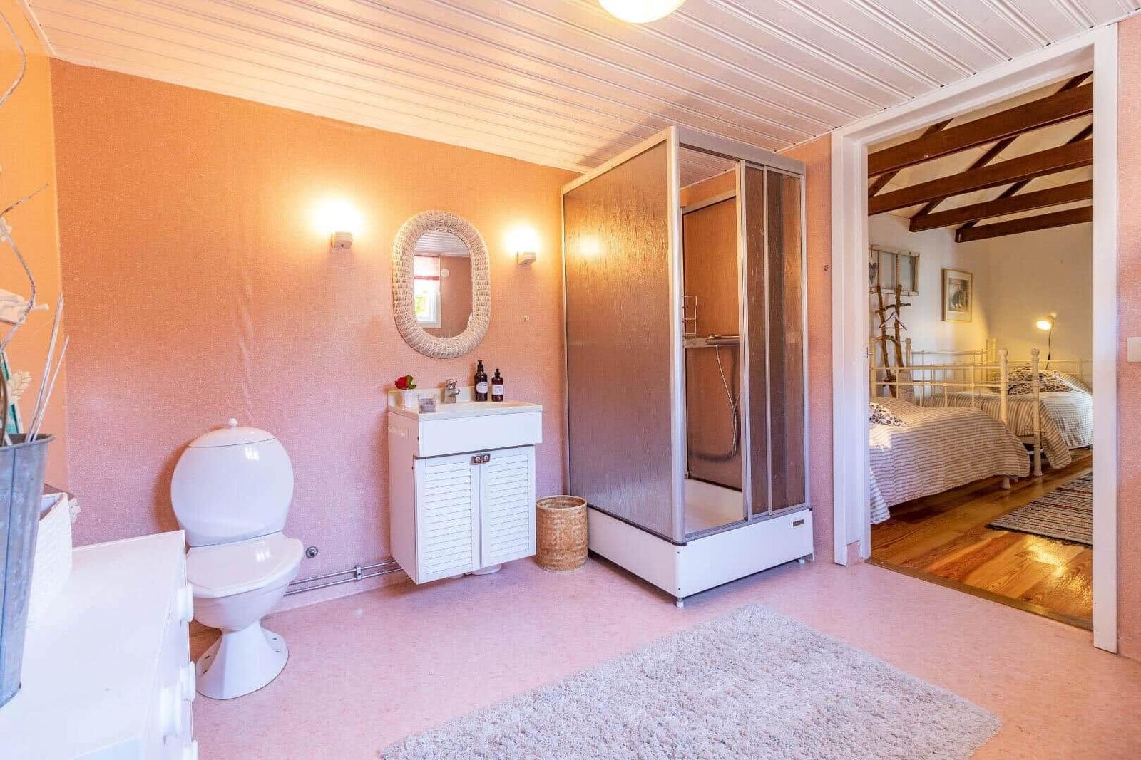Badezimmer mit Dusche, Waschbecken und Toilette. Blick in das Schlafzimmer mit zwei Betten.