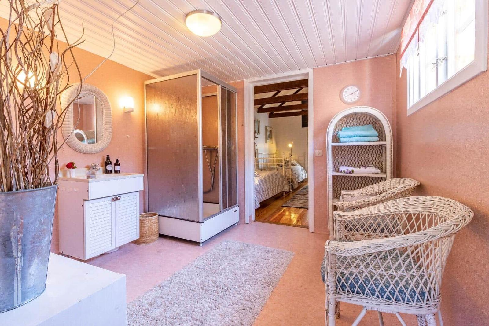 Ein Raum mit Dusche, Waschbecken und Stühlen. Durchgang in Schlafzimmer mit Bett.